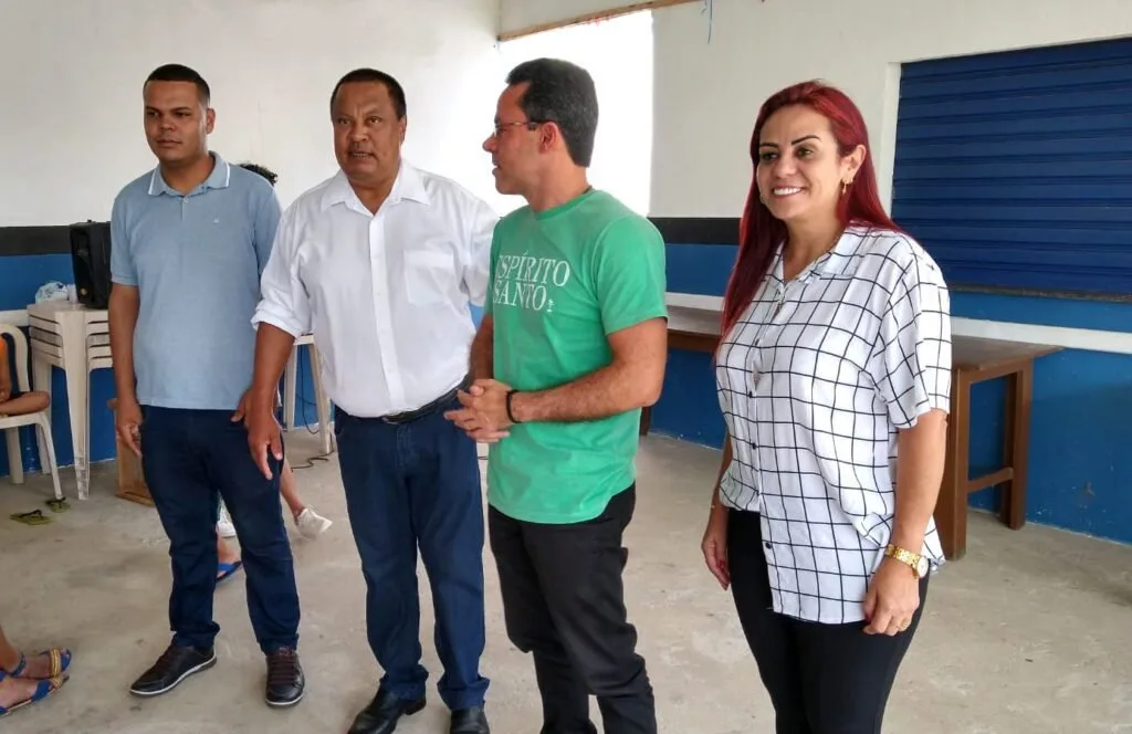 Grupo de cinco pessoas conversa em pé dentro de salão claro durante encontro