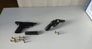 Pistola, revólver e munições apreendidos dispostos sobre superfície clara