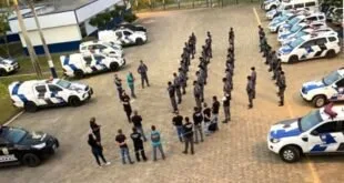 Vista do alto de policiais em formação em pátio ao lado de viaturas brancas
