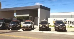 Viaturas policiais estacionadas em frente a prédio com portaria e muro claro