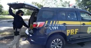 Agentes inspecionam o porta-malas aberto de uma viatura da PRF em pátio