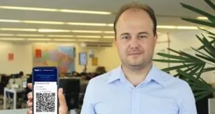 Homem de camisa azul segura celular com aplicativo aberto em escritório