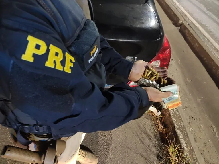 Agente com colete escrito PRF abre pacote apreendido em acostamento de estrada