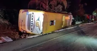 Ônibus tombado com a marca Gontijo à beira da pista durante a noite