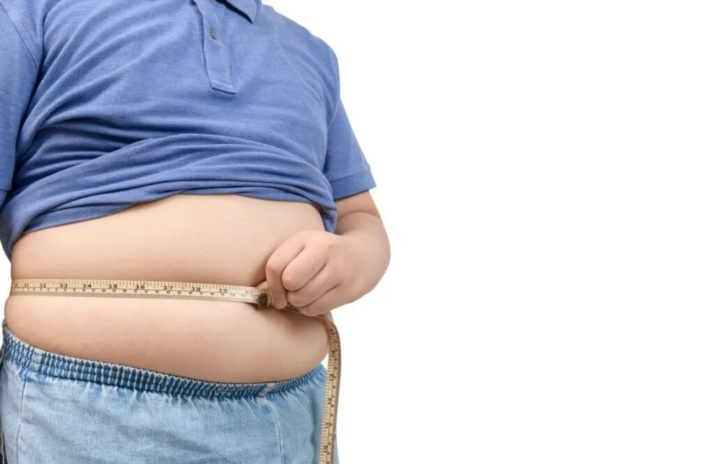 Homem de camisa azul segura dobra de gordura na barriga, imagem ilustrativa sobre obesidade