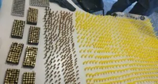 Munições enfileiradas sobre superfície clara ao lado de peças de roupa dobradas