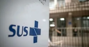 Banner com a logomarca do SUS em frente à fachada de unidade de saúde