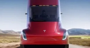 Caminhão elétrico vermelho de cabine arredondada visto de frente com faróis acesos