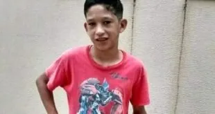 Adolescente de camiseta vermelha sorrindo em frente a uma parede clara