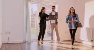 Mulher com prancheta recebe casal em sala vazia de imóvel, imagem ilustrativa sobre moradia