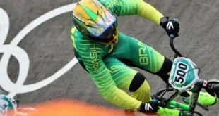 Ciclista de uniforme verde e amarelo inclinado em curva de pista de bicicross