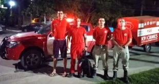 Quatro bombeiros de uniforme vermelho posam à noite com cão ao lado de viatura K9