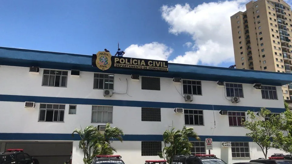 Fachada de prédio com letreiro 'Polícia Civil' e viaturas estacionadas em frente