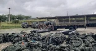 Militares ao lado de caminhões do Exército e pilhas de sacos escuros empilhados no chão