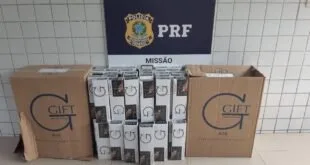Maços de cigarro empilhados diante de banner da PRF com o brasão do órgão