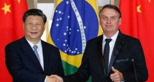 Dois homens de terno apertam as mãos diante das bandeiras do Brasil e da China