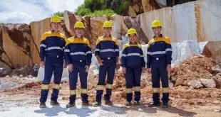 Grupo de trabalhadores de uniforme e capacete amarelo posa diante de pedreira