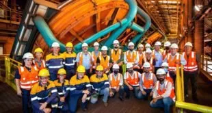 Grupo de trabalhadores de capacete e colete refletivo posando dentro de uma planta industrial
