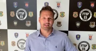 Homem de camisa azul diante de painel com brasões de instituições policiais