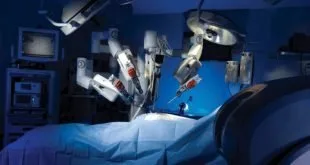 Braços de robô cirúrgico posicionados sobre paciente coberto por campo azul em sala de cirurgia