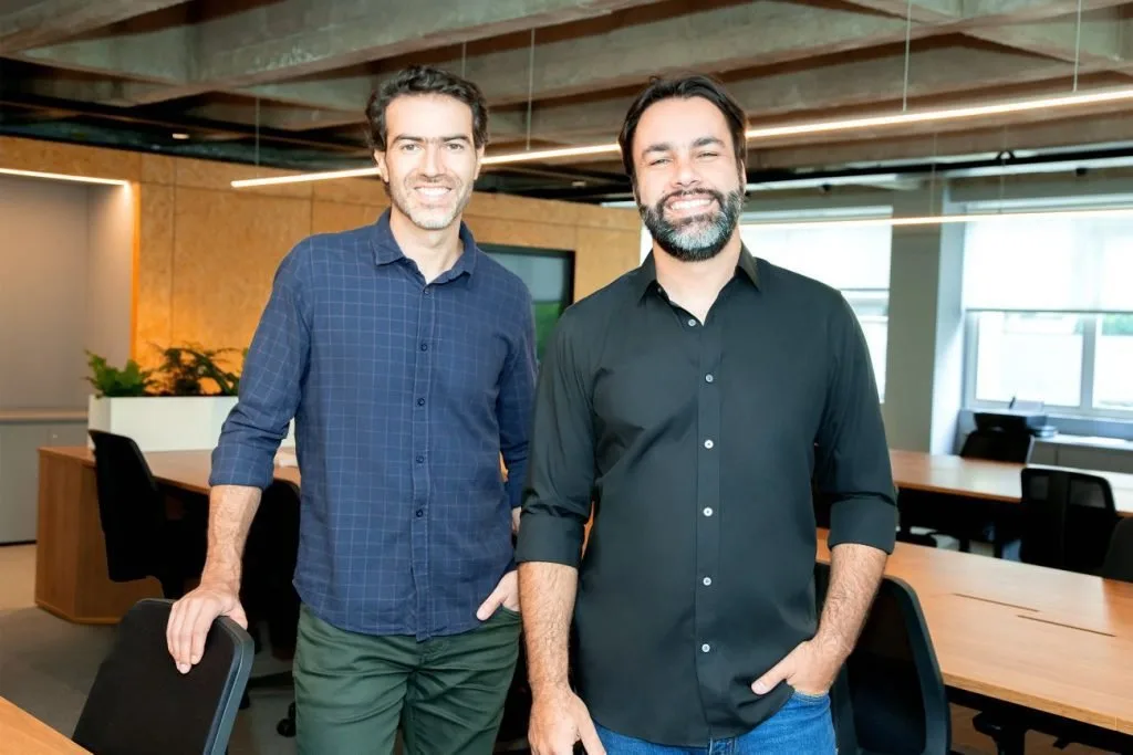 Dois homens de camisa escura posam lado a lado em ambiente de escritório