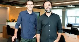 Dois homens de camisa escura posam lado a lado em ambiente de escritório