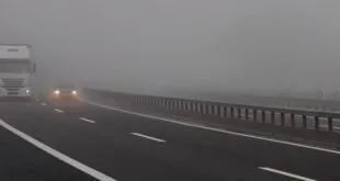 Rodovia tomada por neblina densa com um carro de faróis acesos ao fundo