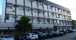Fachada de prédio público de três andares com carros estacionados no pátio
