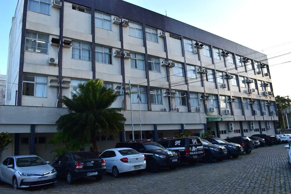 Fachada de prédio público de três andares com carros estacionados no pátio