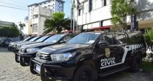 Viaturas da Polícia Civil enfileiradas em estacionamento diante de prédio