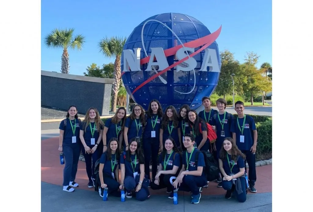 Grupo de estudantes uniformizados posando diante do letreiro e do globo da NASA