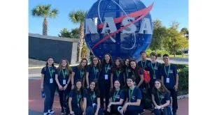 Grupo de estudantes uniformizados posando diante do letreiro e do globo da NASA