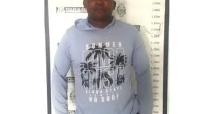 Homem de moletom claro em pé diante de painel de identificação de delegacia