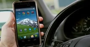 Mão segurando celular ao volante de um carro, imagem ilustrativa sobre trânsito