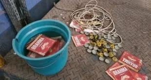 Balde com rótulos de cerveja e tampinhas espalhadas no chão ao lado de fios