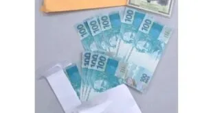 Cédulas de cem reais ao lado de um envelope pardo e embalagens plásticas sobre mesa