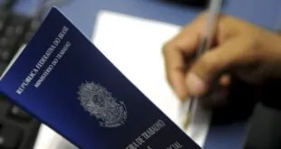 Carteira de Trabalho e Previdência Social azul ao lado de mão preenchendo um formulário