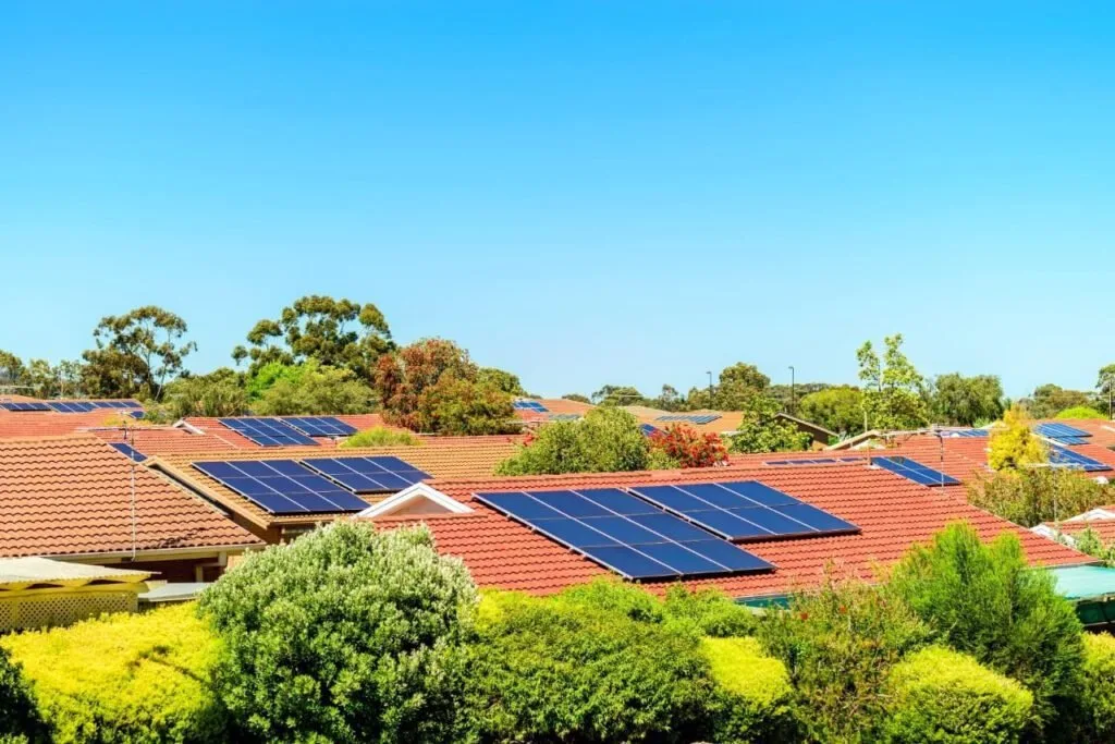 Placas solares instaladas em telhados de casas em bairro arborizado sob céu azul