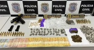 Drogas, munições e dinheiro dispostos sobre mesa diante de banners da Polícia Civil