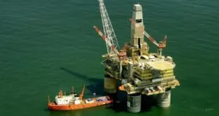 Plataforma de petróleo em alto-mar ao lado de navio de apoio laranja em água esverdeada