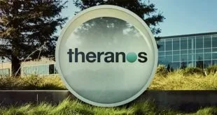 Totem de concreto com o logotipo 'theranos' em jardim diante de prédio