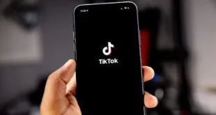 Mão segurando celular com a tela inicial do aplicativo TikTok