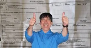 Homem de camisa azul faz sinal de positivo sobre notificação de infração de trânsito de Guarapari