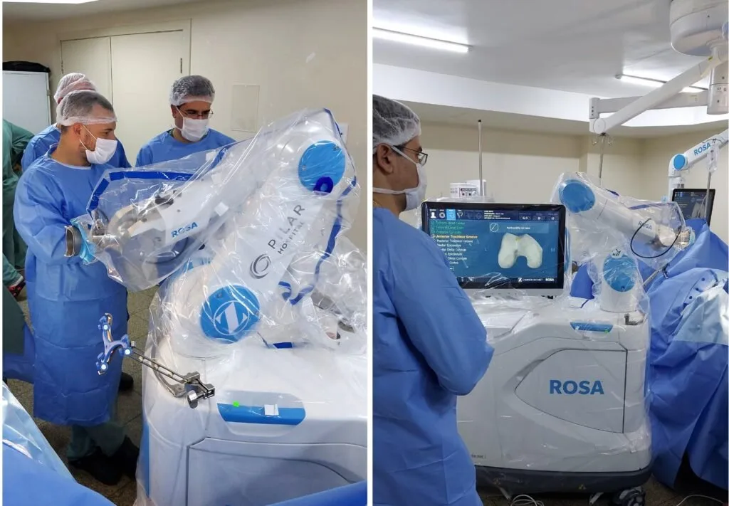 Equipe médica de avental azul manipulando braço robótico cirúrgico em centro cirúrgico