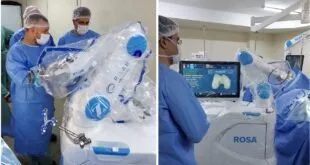 Equipe médica de avental azul manipulando braço robótico cirúrgico em centro cirúrgico