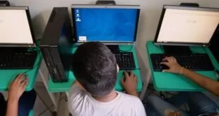 Estudante visto de costas usando computador de mesa em laboratório de informática