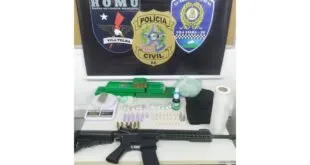 Fuzil, munições, drogas e balança sobre mesa diante de banner da Guarda Municipal de Vila Velha