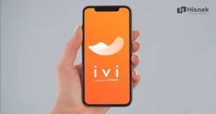 Mão segurando celular com tela laranja de aplicativo aberta sobre fundo cinza claro
