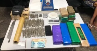 Tabletes e porções de entorpecentes, celulares e emblema policial sobre mesa branca