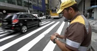 Agente de trânsito de boné amarelo anotando em bloco ao lado de faixa de pedestres